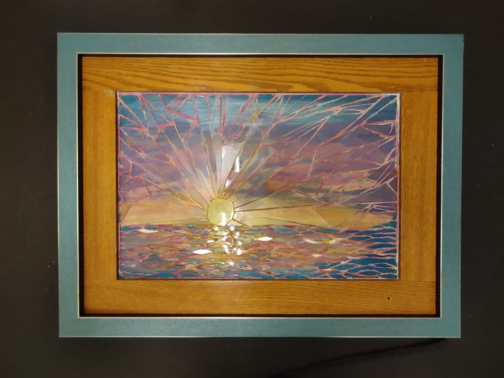 Mockzaic of a sunset, with pink blue and yellow sky,  reflection in the sea and golden oak and blue aluminum frame.